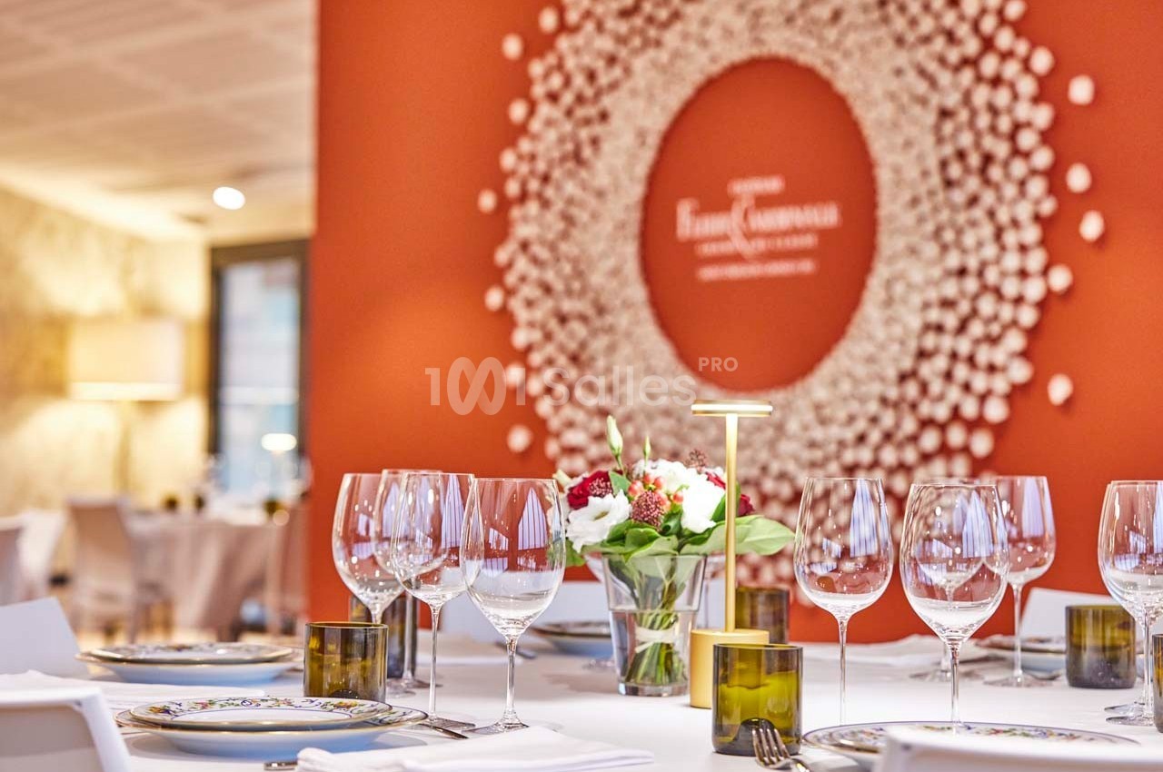 Salle de restaurant élégante avec tables dressées, décorée d'un mur rouge orné d'une œuvre circulaire en relief.