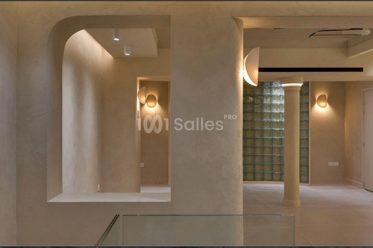 Intérieur minimaliste avec murs beige texturés, éclairage mural doux et cloison en briques de verre.