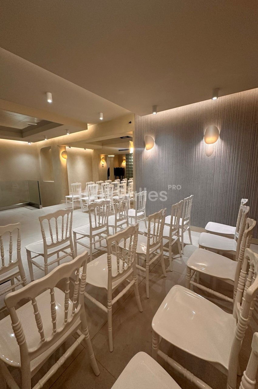 Salle lumineuse avec des chaises blanches alignées, murs texturés et éclairage mural discret.