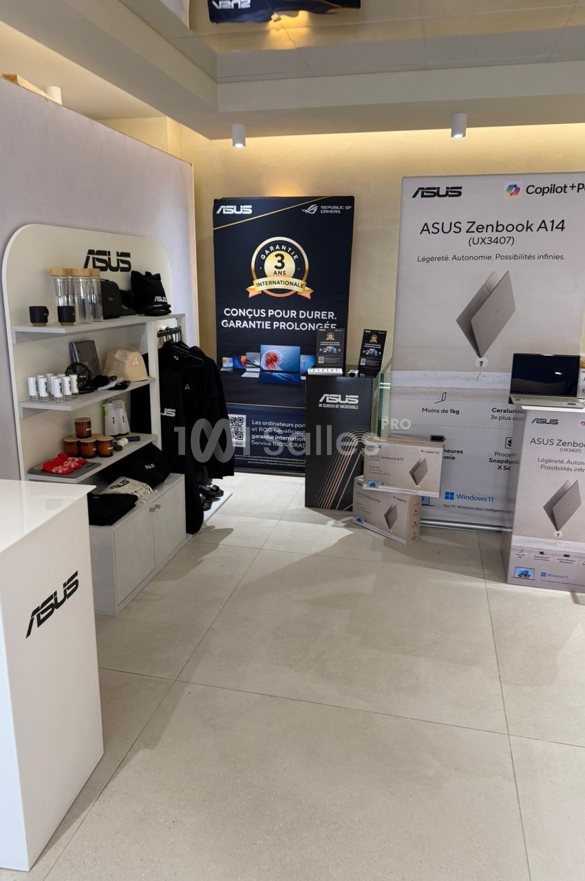 Stand promotionnel ASUS présentant des ordinateurs portables, accessoires et affiches publicitaires dans un espace lumineux.