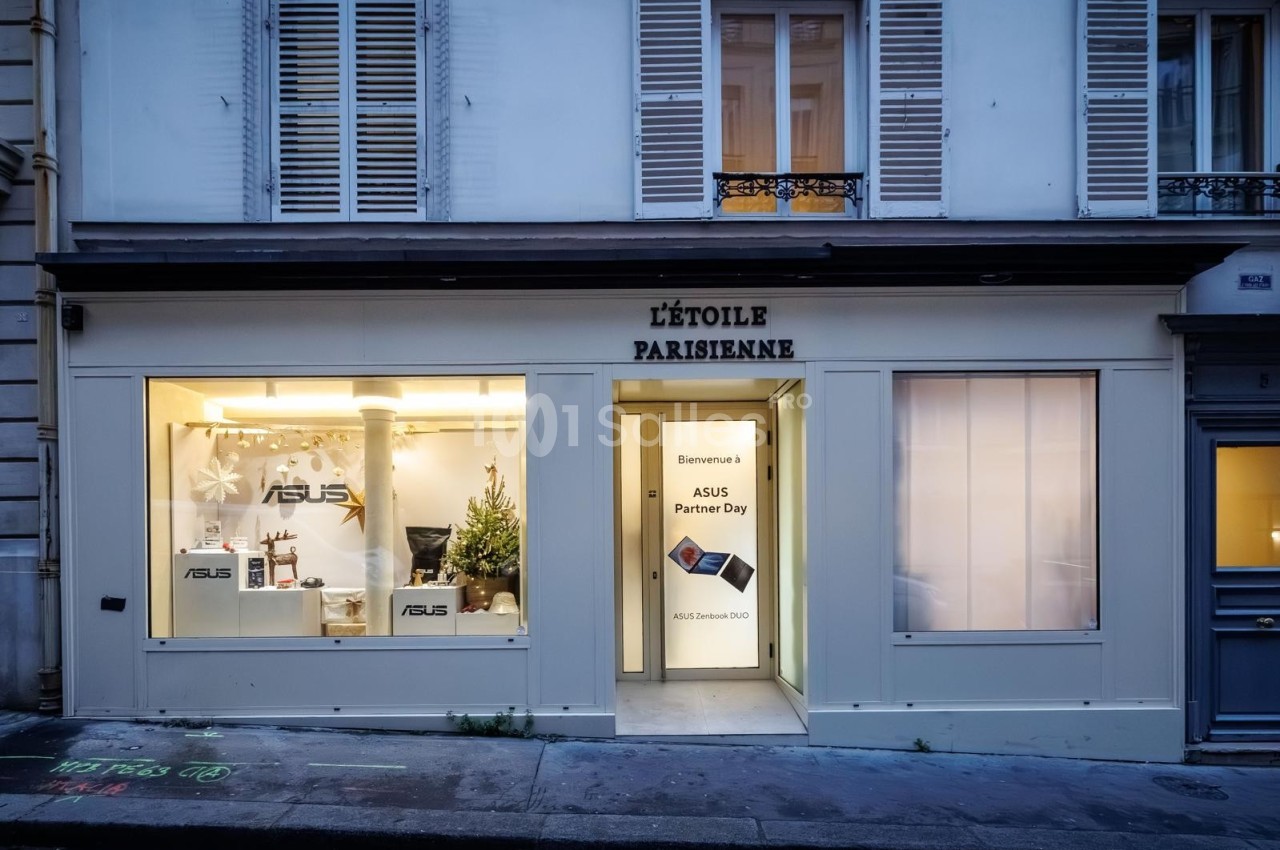 Façade d'une boutique avec vitrines éclairées, affichant des produits ASUS et une pancarte d'accueil pour un événement.