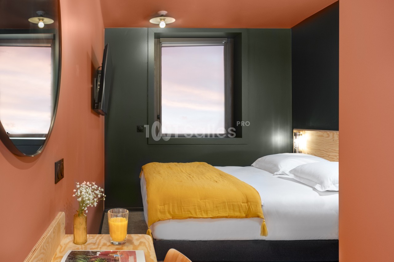Chambre moderne avec lit double, murs orange, fenêtre avec vue sur le ciel, bureau en bois et décoration minimaliste.