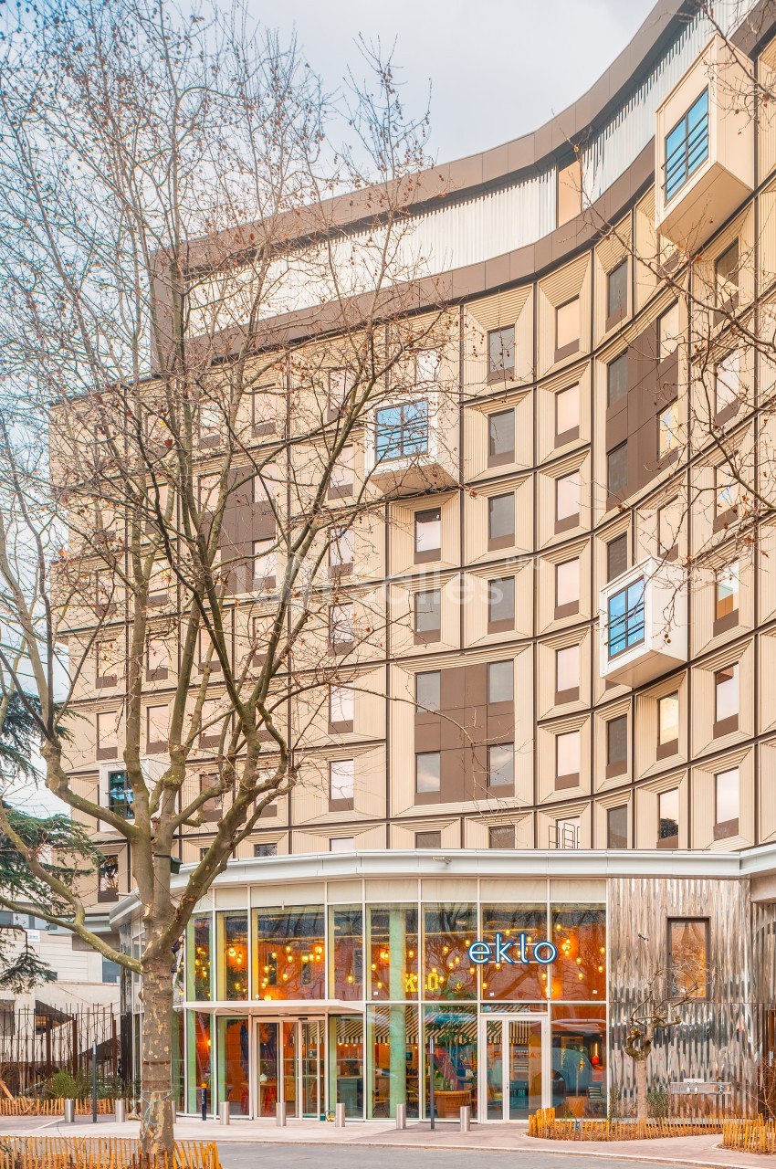 Façade d'un bâtiment moderne avec de grandes fenêtres, des arbres devant et une entrée vitrée portant le nom ’Eklo’.