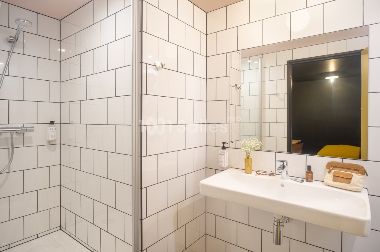 Salle de bain moderne avec douche à l'italienne, carrelage blanc, lavabo suspendu et miroir éclairé.