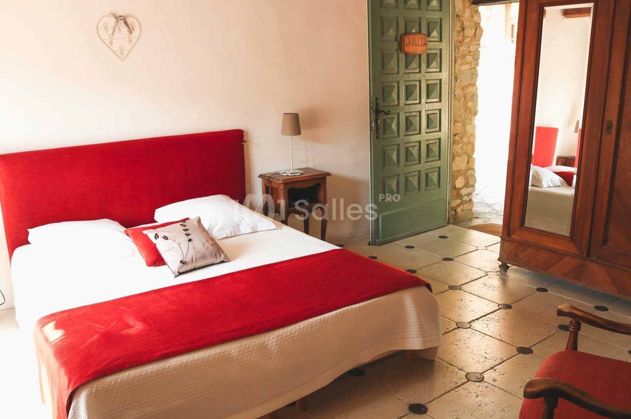 Chambre lumineuse avec lit double, tête de lit rouge, armoire en bois et porte verte ouverte sur un couloir.