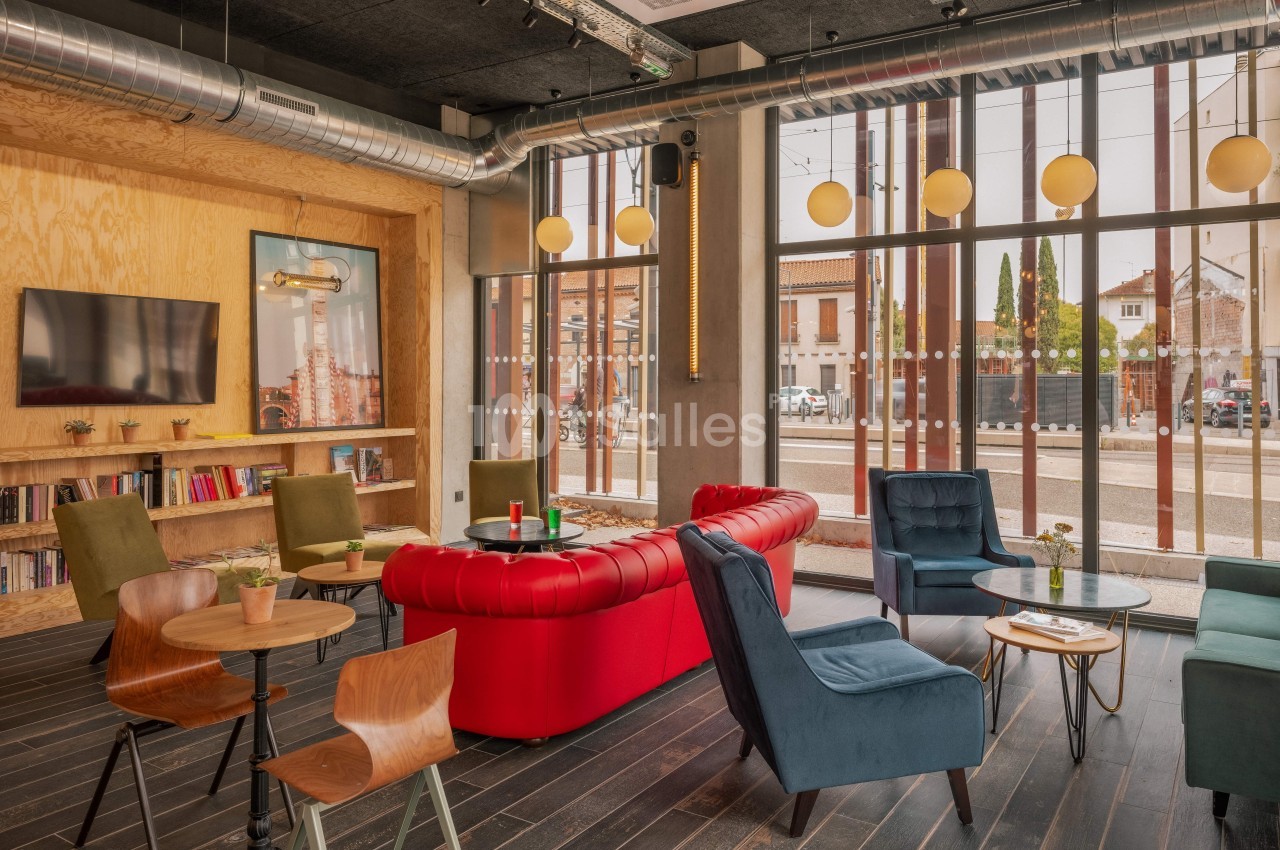 Espace lounge lumineux avec canapés, fauteuils colorés, tables en bois et grande baie vitrée donnant sur l'extérieur.