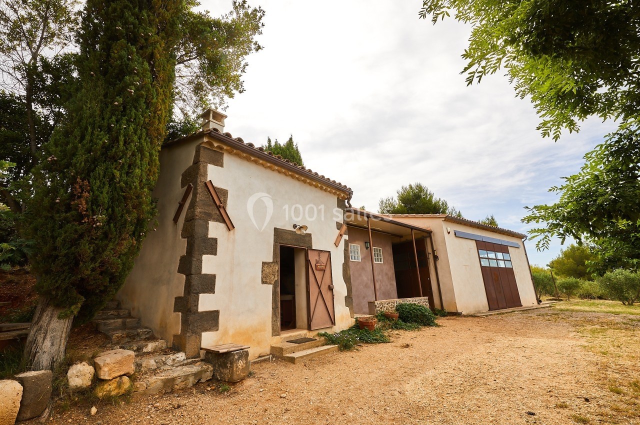 Bâtiment rural en pierre avec porte en bois, entouré de végétation et situé sur un terrain en terre battue.