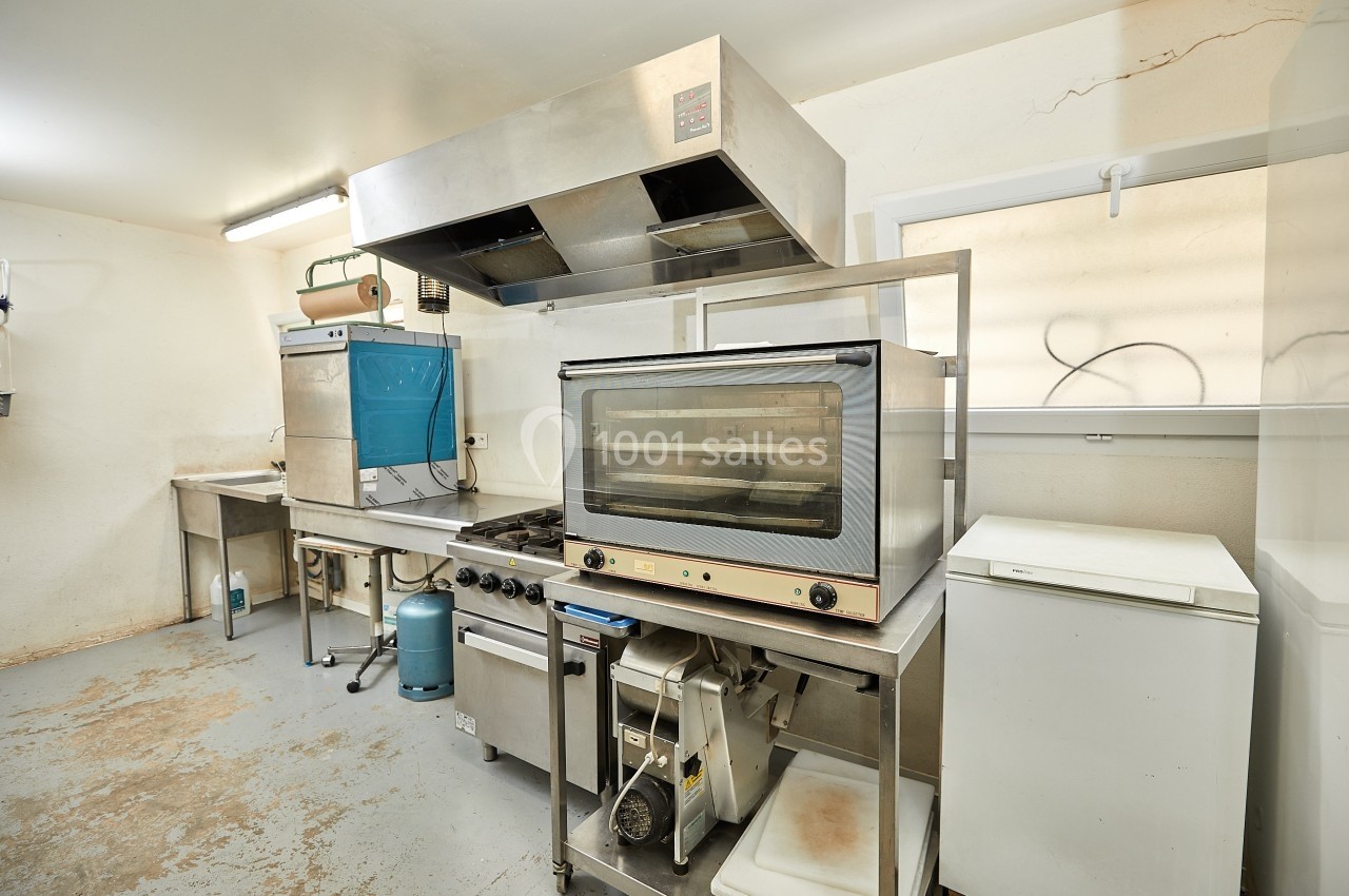 Cuisine professionnelle équipée avec four, hotte, réfrigérateur et plans de travail en acier inoxydable.