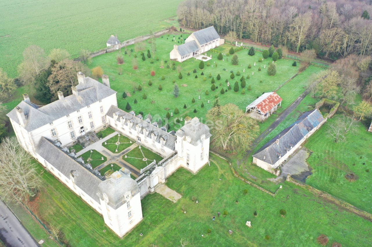 Vue aérienne d'un château entouré de jardins, de bâtiments annexes et de prairies verdoyantes.