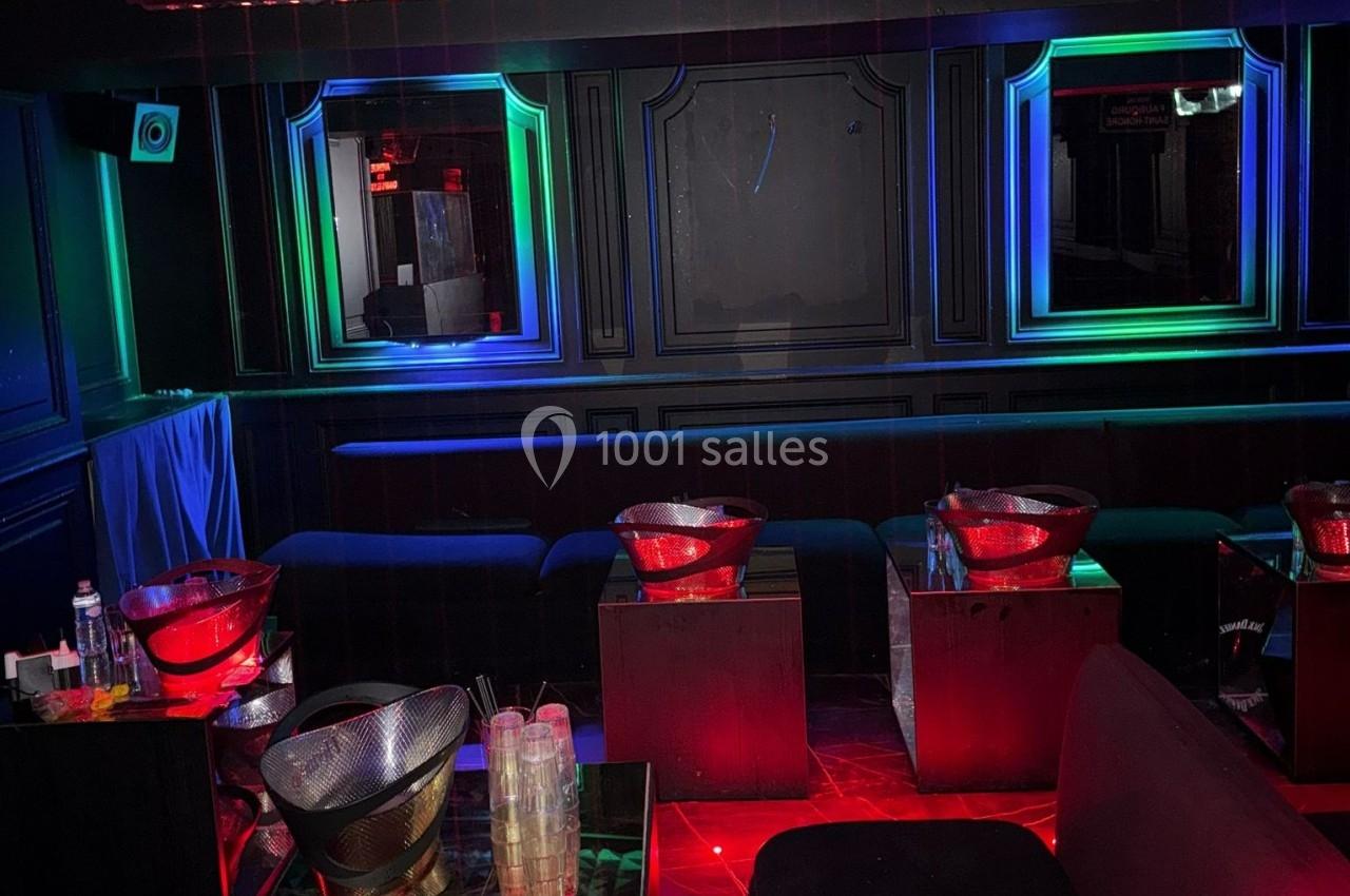 Salle sombre avec banquettes, tables basses et éclairage coloré rouge, bleu et vert créant une ambiance festive.
