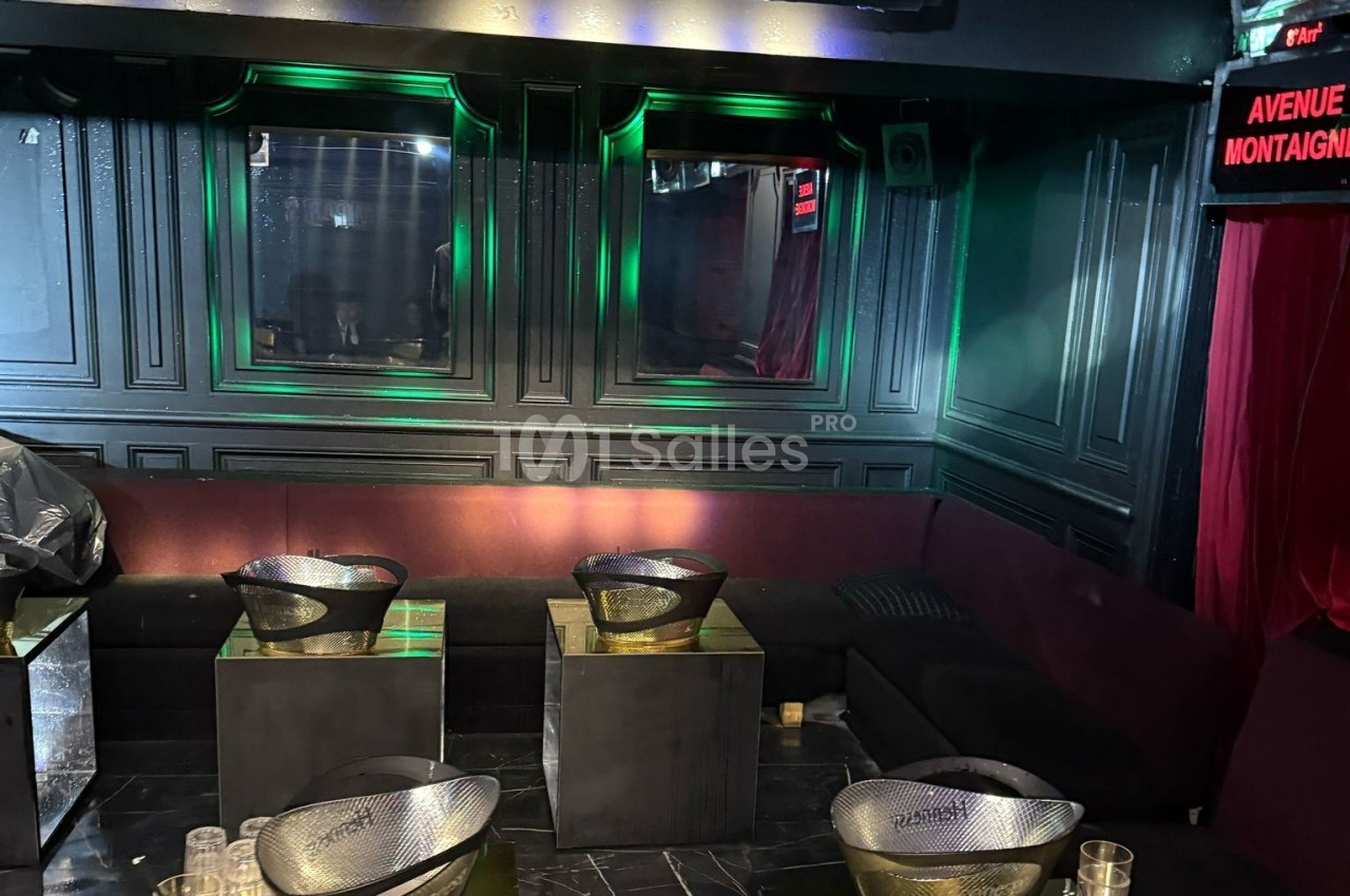Banquettes noires et violettes entourant des tables basses avec des seaux à champagne dans un espace sombre et éclairé.