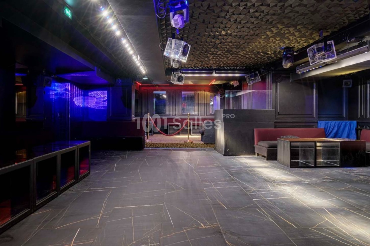 Salle de discothèque vide avec éclairage tamisé, piste de danse en marbre sombre et banquettes rouges.