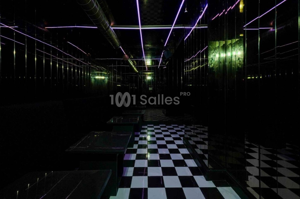 Salle sombre avec sol en damier noir et blanc, murs réfléchissants et éclairage néon violet au plafond.