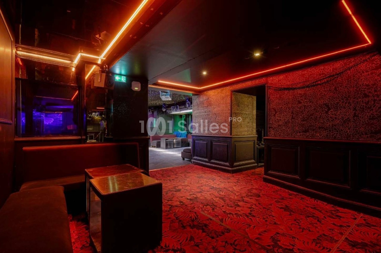 Salle intérieure avec banquettes, table basse, éclairage rouge et décorations sombres, donnant sur un espace ouvert.
