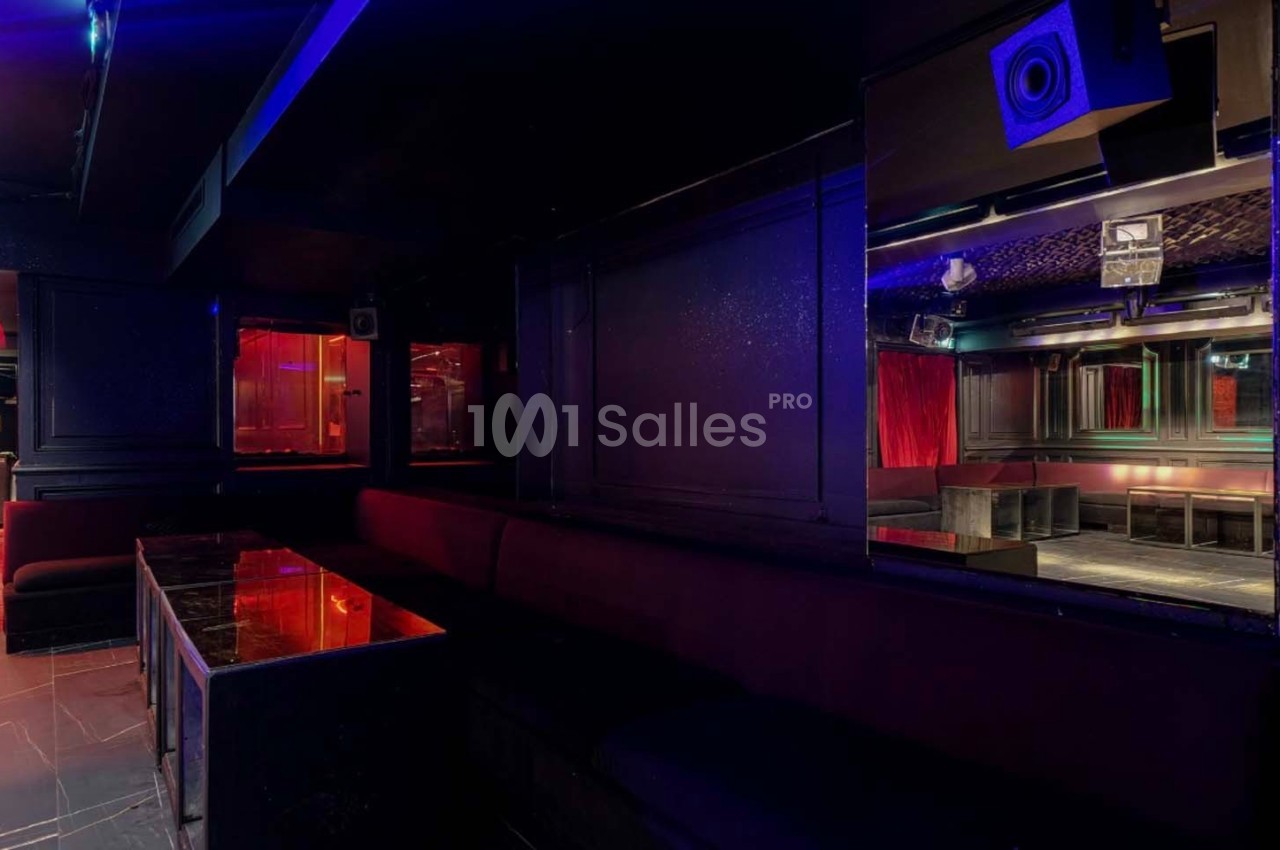 Salle sombre avec banquettes rouges, tables en marbre noir et éclairage tamisé aux tons rouges et bleus.