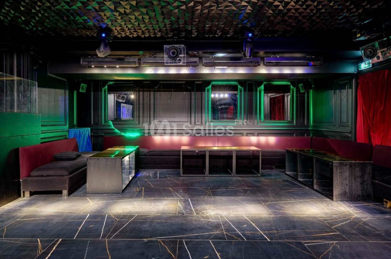 Salle de club vide avec banquettes rouges, tables basses, éclairage tamisé et plafond texturé.