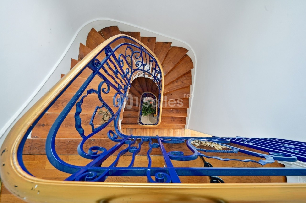 Escalier en colimaçon en bois avec une rampe en métal bleu et doré, vu en plongée depuis le haut.