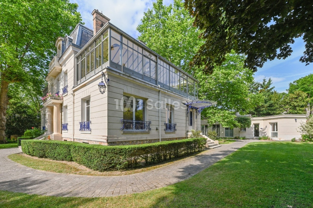 Grande maison de style classique avec véranda, entourée d'un jardin arboré et d'une allée pavée.