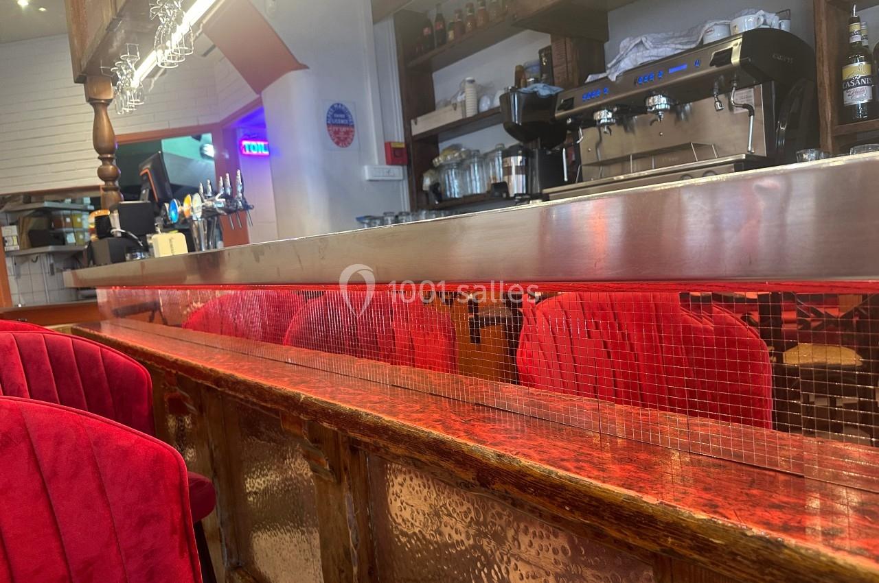 Comptoir de bar en bois avec surface rouge, chaises rembourrées rouges et machine à café en arrière-plan.