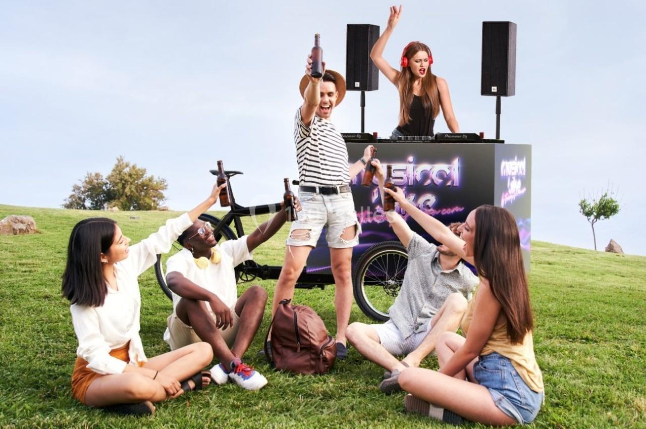 Un groupe de jeunes assis sur l'herbe fête devant une DJ jouant de la musique en plein air.