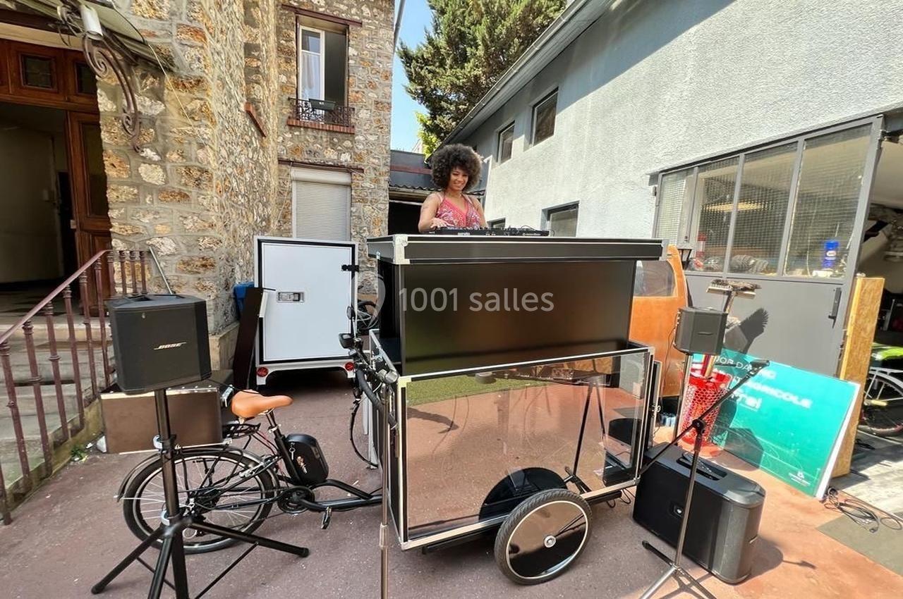 Une DJ joue de la musique sur une scène mobile montée sur un vélo, dans une cour extérieure.