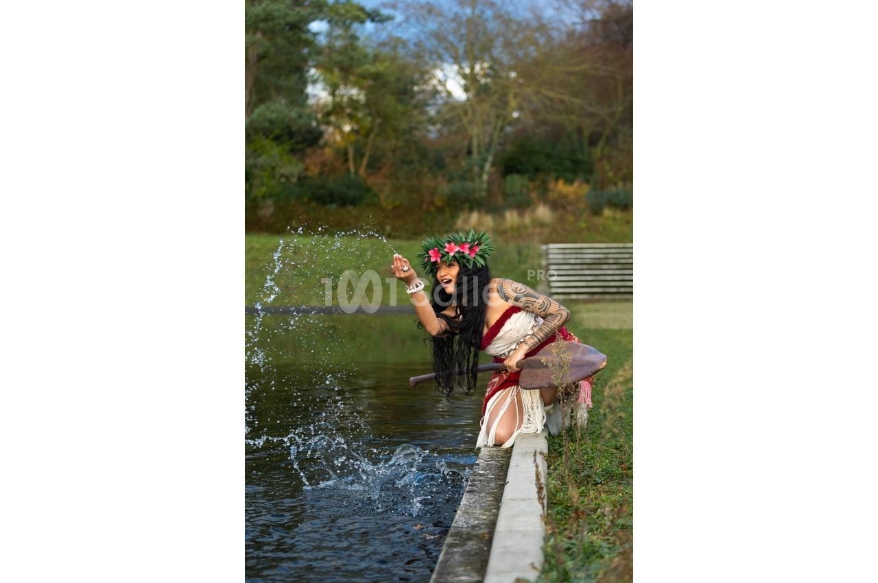 Une femme en tenue traditionnelle éclabousse l'eau d'un bassin en extérieur, entourée de végétation.