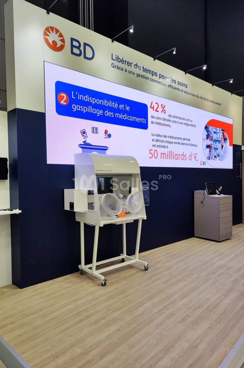 Stand d'exposition avec un écran affichant des données sur la gestion des médicaments et un équipement médical en avant-plan.