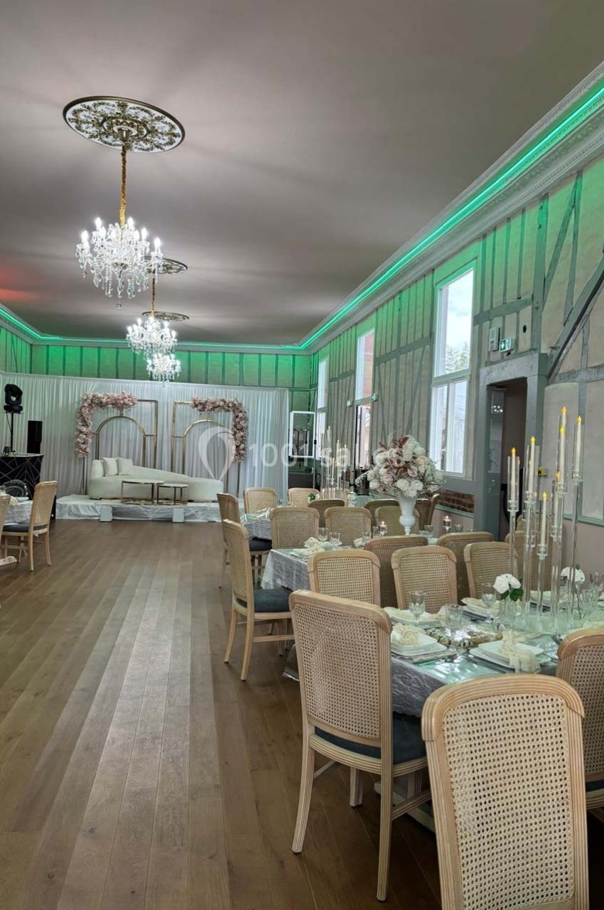 Salle de réception élégante avec tables dressées, chaises en rotin, lustres et décoration florale.