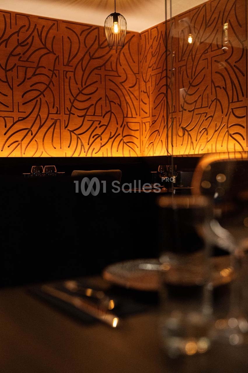 Salle de restaurant avec éclairage tamisé, mur décoratif en bois sculpté et table dressée au premier plan.