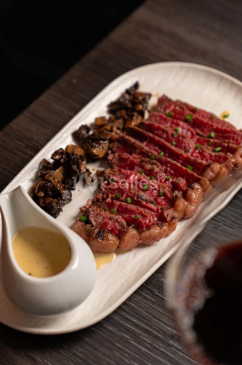 Tranches de viande saignante servies avec des champignons sautés et une sauce dans un récipient en céramique blanche.