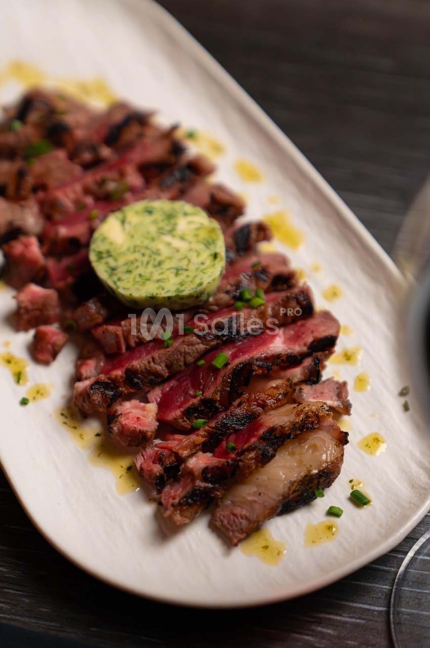 Tranches de steak grillé garnies de beurre aux herbes, servies sur une assiette blanche avec une sauce légère.