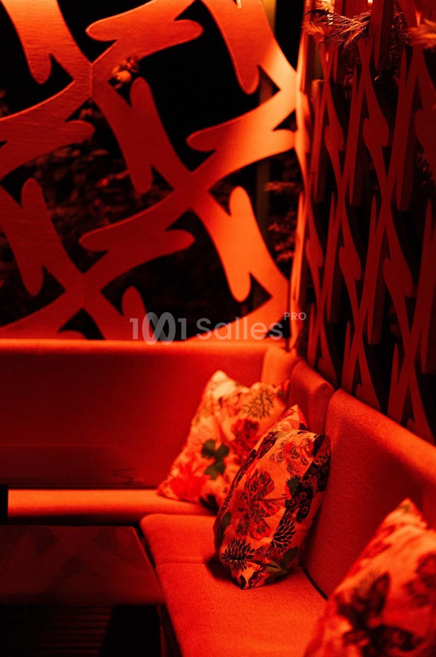 Banquette rouge avec coussins à motifs floraux, entourée de panneaux décoratifs éclairés par une lumière rouge.