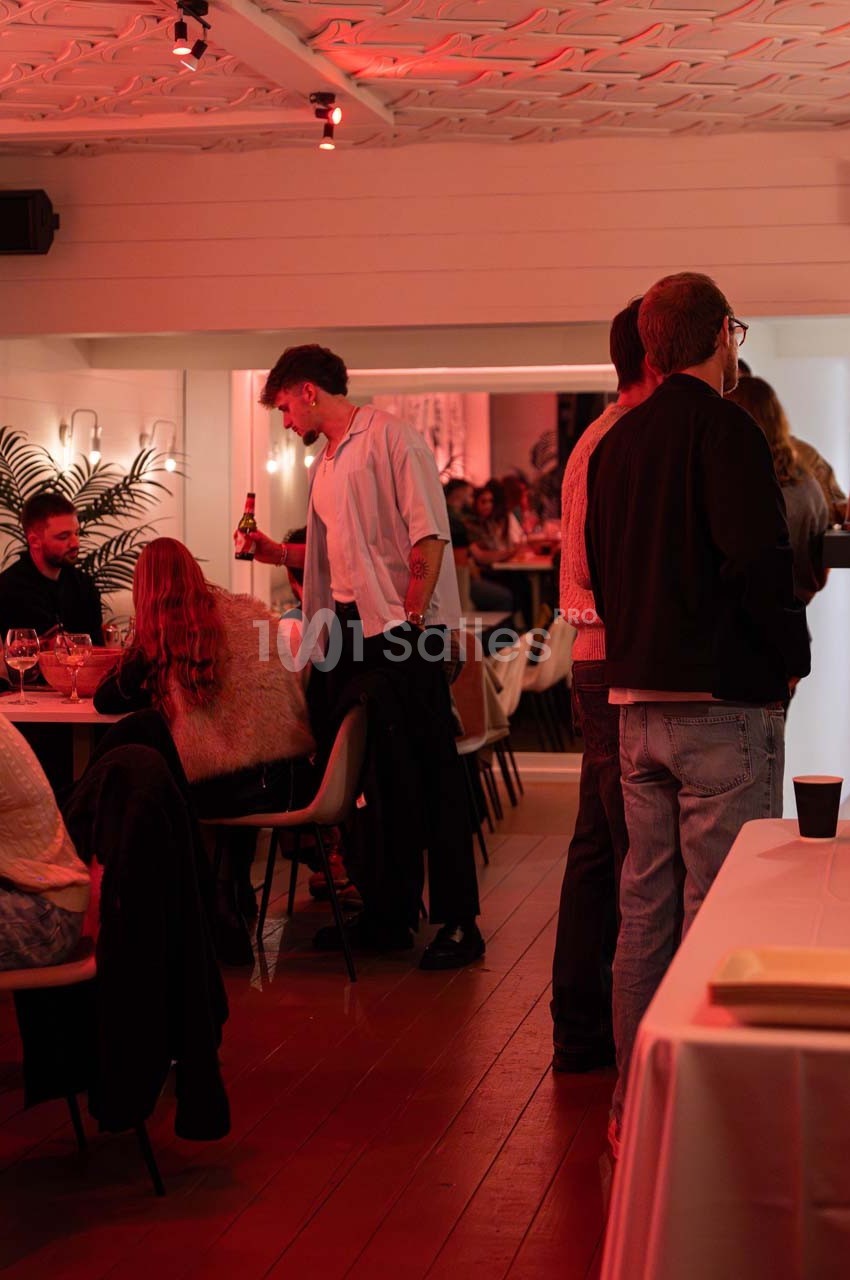 Personnes discutant et partageant des boissons dans un espace intérieur éclairé par une lumière rouge tamisée.
