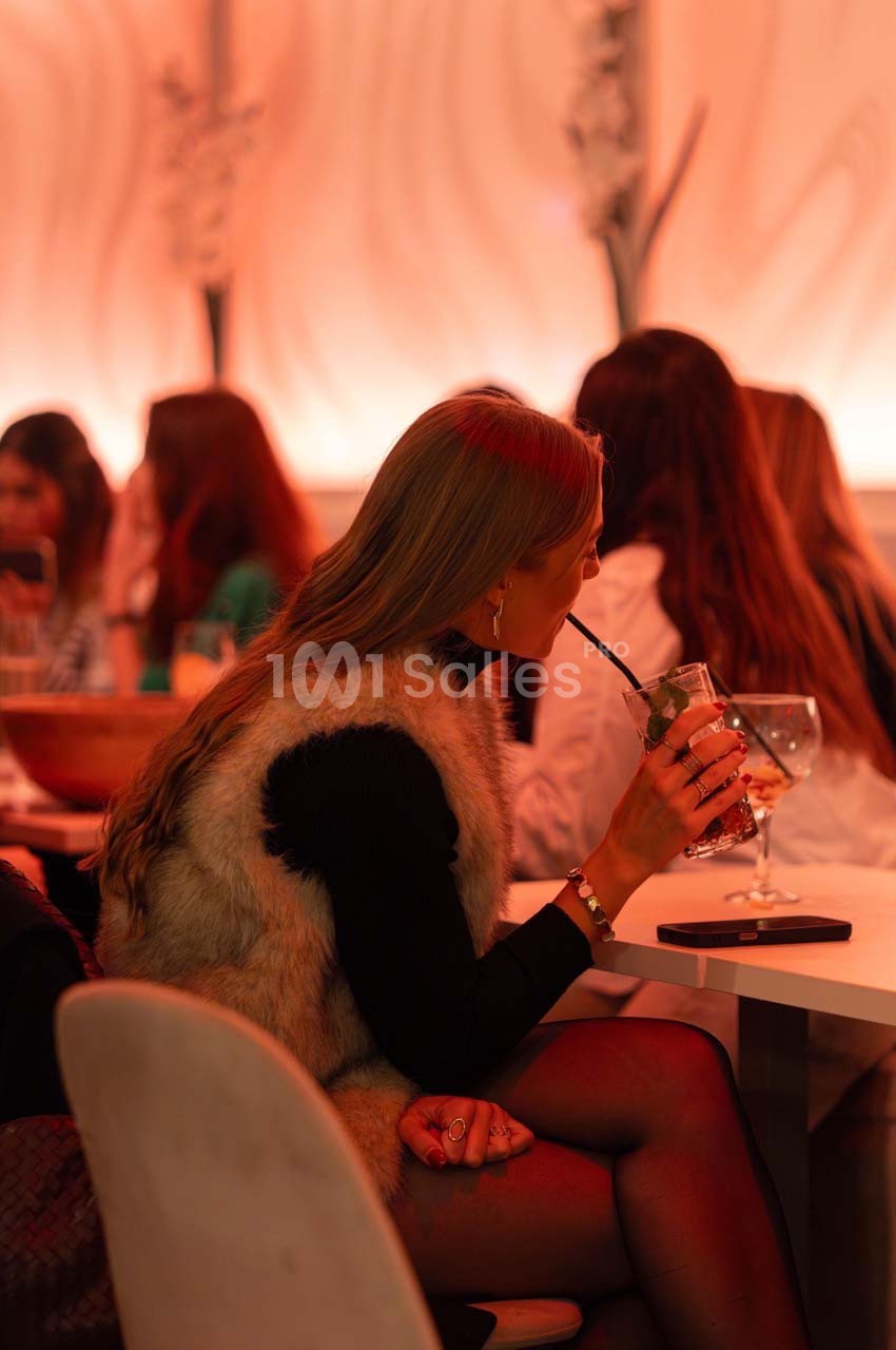 Une femme assise dans un restaurant, buvant une boisson avec une paille, entourée d'autres clients.