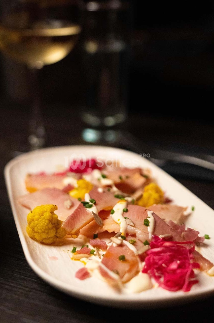 Assiette de charcuterie avec jambon, chou-fleur jaune, chou rouge mariné, crème et ciboulette, servie sur une table sombre.
