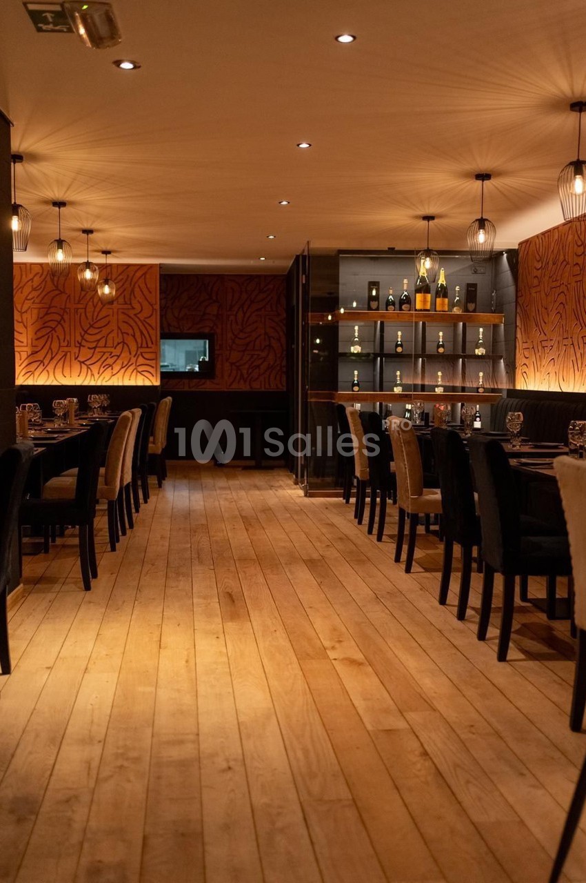 Salle de restaurant chaleureuse avec parquet en bois clair, murs décorés et étagères contenant des bouteilles.