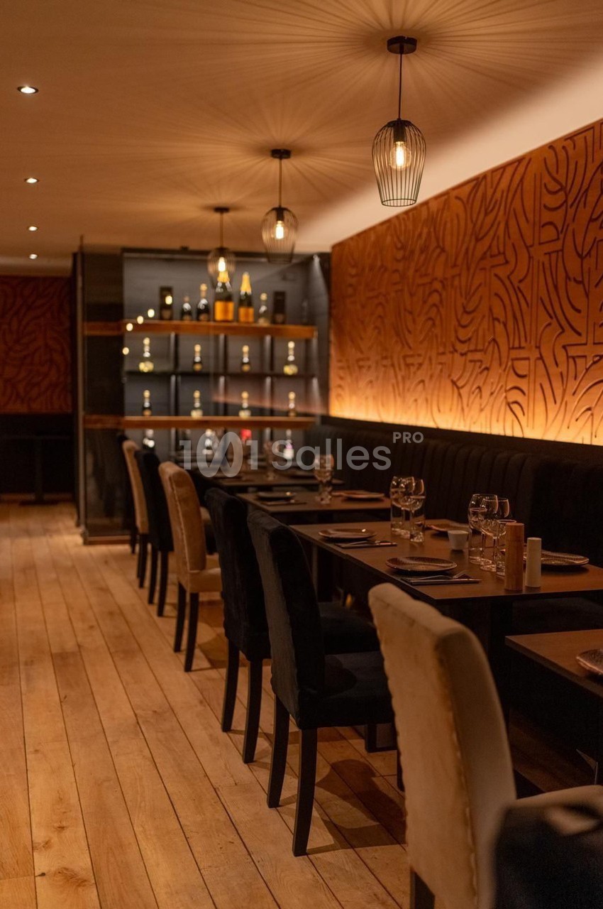 Salle de restaurant chaleureuse avec tables dressées, éclairage tamisé et décoration murale en bois sculpté.