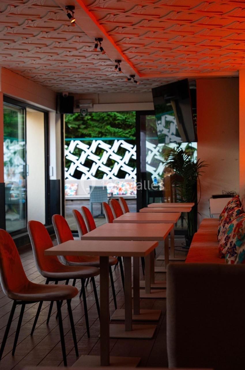 Salle de restaurant moderne avec tables alignées, chaises colorées et terrasse visible à travers des baies vitrées.