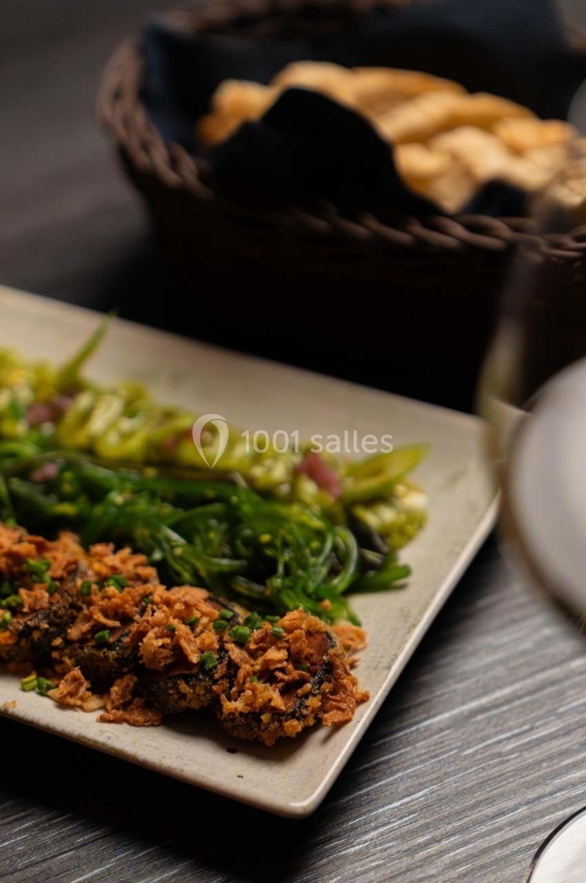 Assiette de légumes verts et beignets croustillants, servie sur une table avec un panier de pain en arrière-plan.