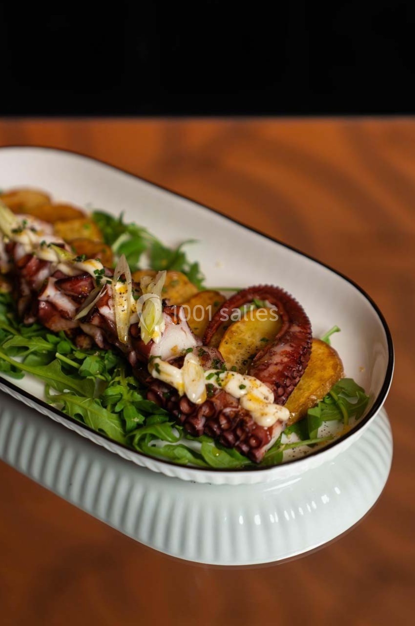 Plat de tentacules de poulpe grillés servis sur un lit de roquette avec des pommes de terre et une garniture d'herbes.