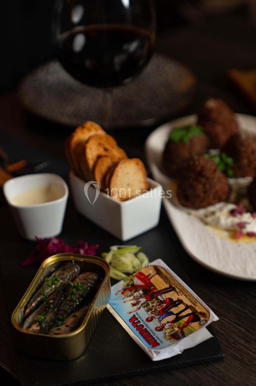 Assiette avec sardines en conserve, crackers, boulettes de viande sur sauce blanche et verre de vin rouge en arrière-plan.