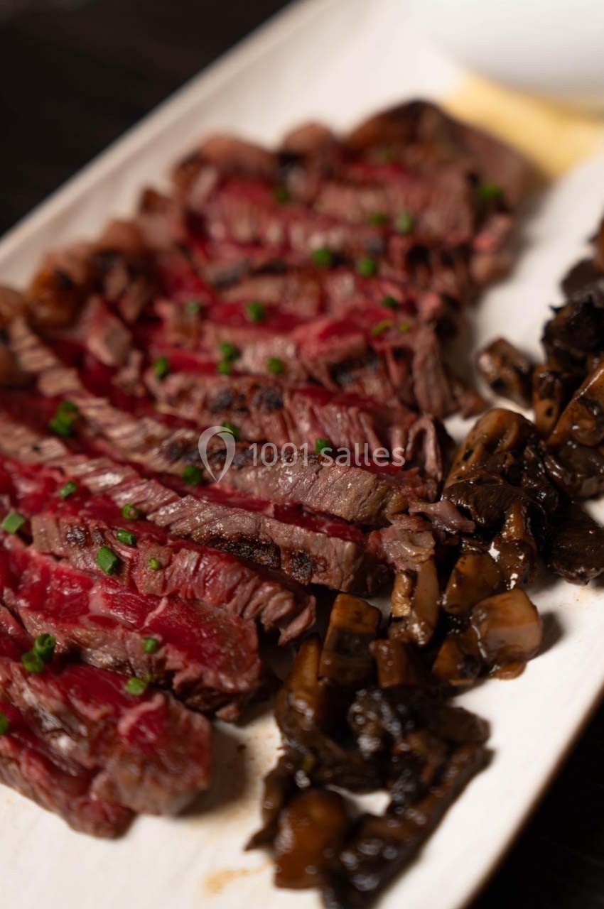 Tranches de steak saignant garnies de ciboulette, accompagnées de champignons sautés sur une assiette blanche.