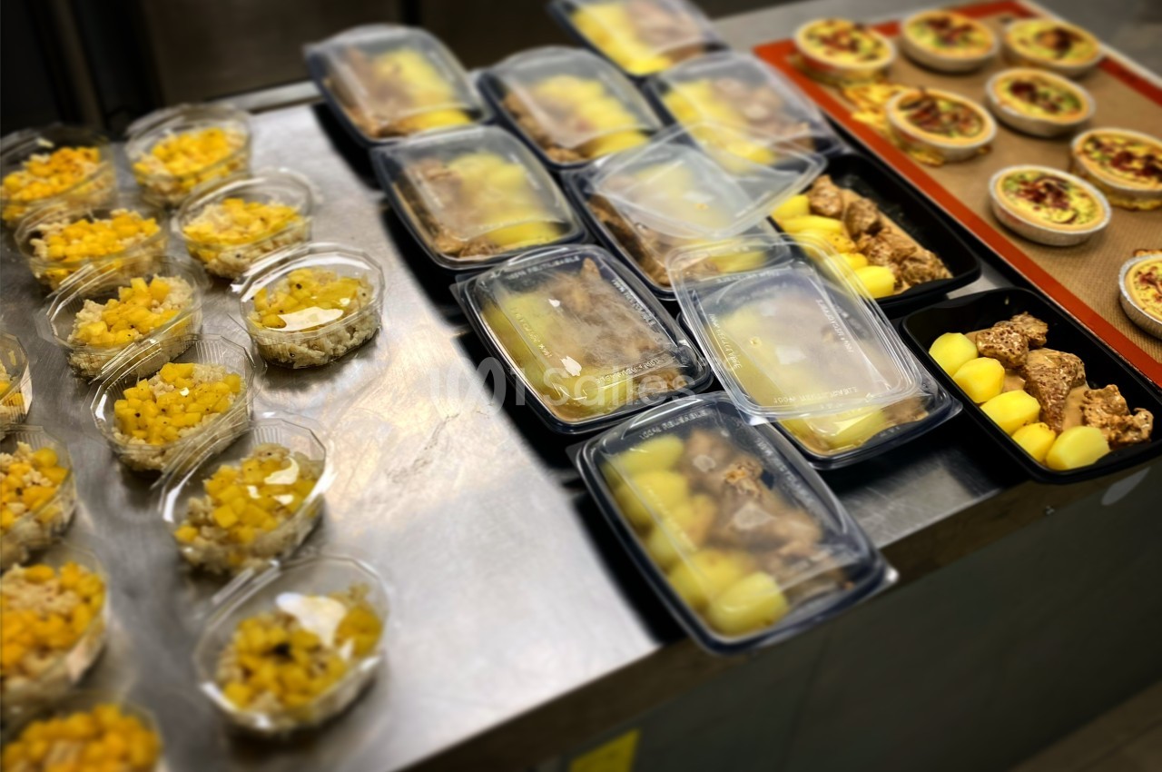 Repas préparés disposés sur un plan de travail, comprenant salades, plats principaux et desserts emballés.