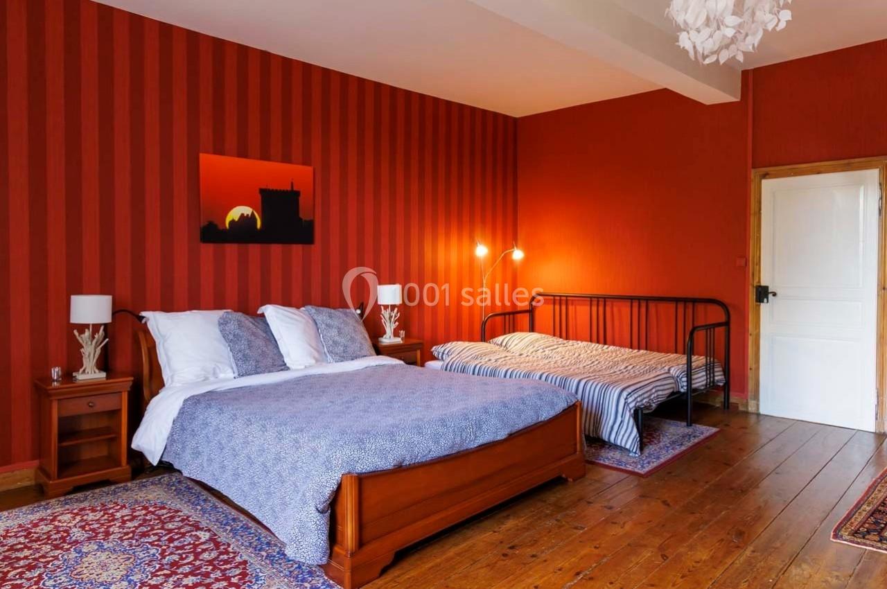Chambre avec murs rouges, lit double, lit simple, lampes de chevet et parquet en bois.
