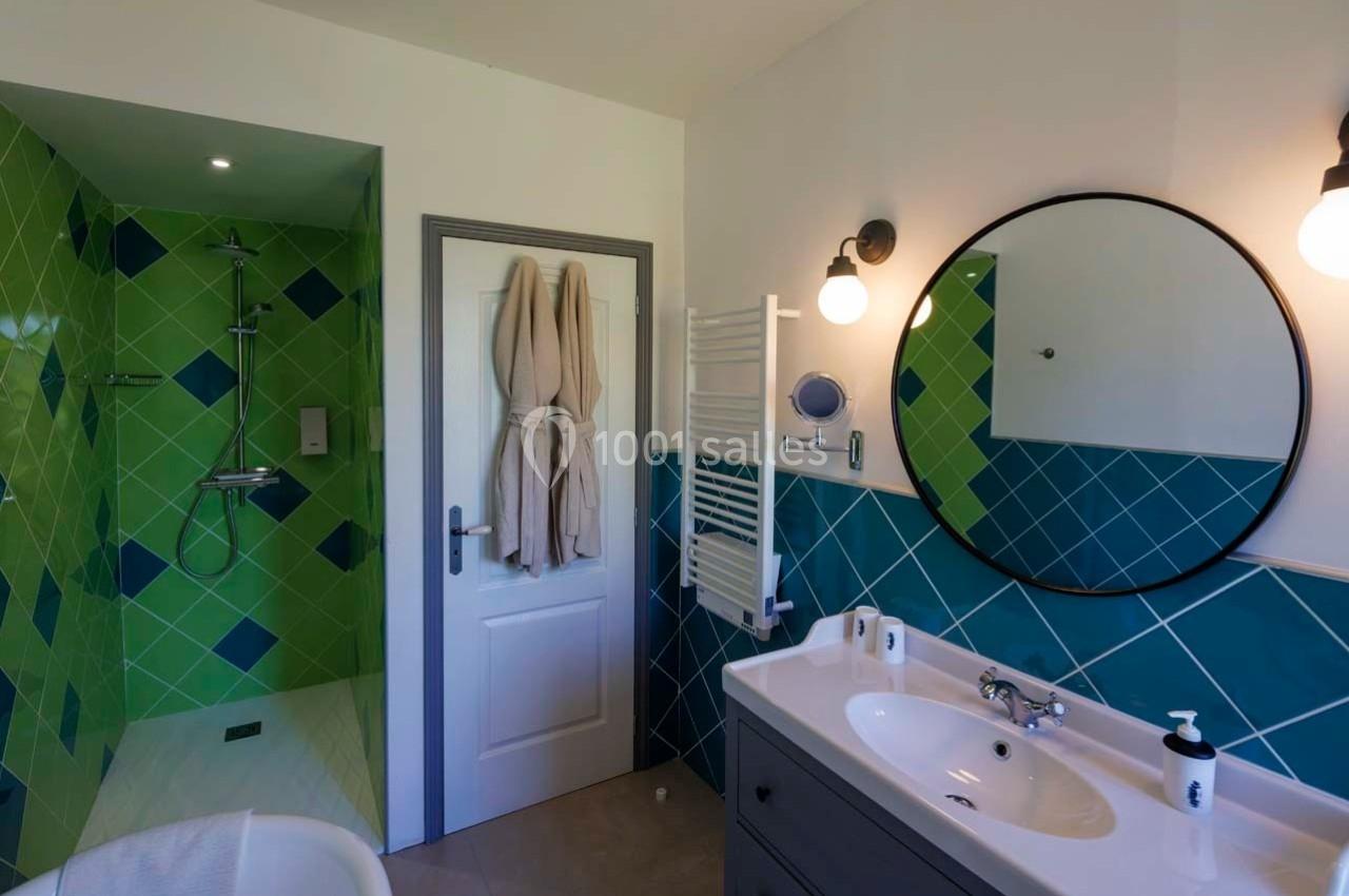 Salle de bain avec douche à l'italienne, carrelage vert, lavabo avec miroir rond et porte-serviettes mural.