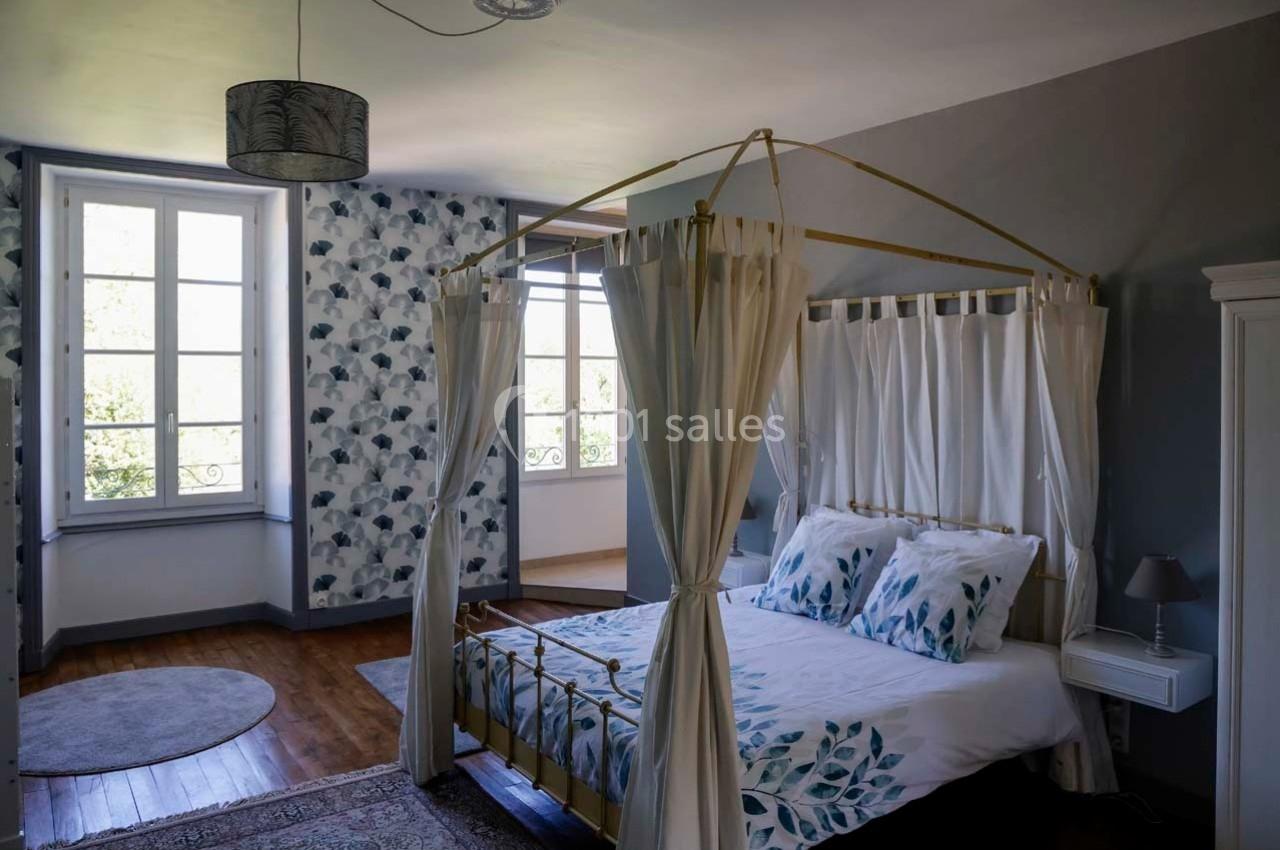 Chambre lumineuse avec lit à baldaquin, draps à motifs floraux, parquet en bois et murs décorés de papier peint.