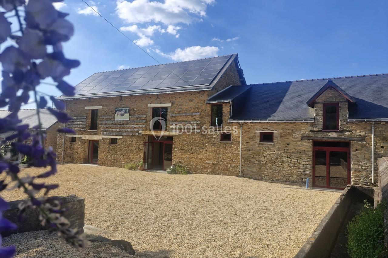 Façade d'une maison en pierre rénovée avec panneaux solaires sur le toit, entourée d'une cour en gravier.