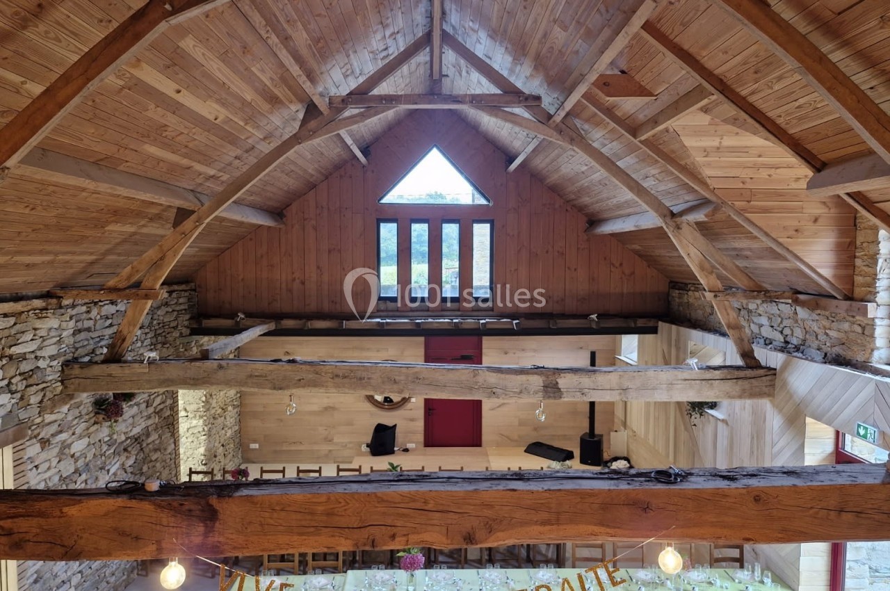 Vue intérieure d'une salle en bois avec poutres apparentes, murs en pierre et une bannière ’Vive la retraite !’ suspendue.