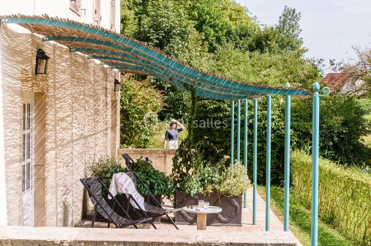 Terrasse ombragée avec mobilier de jardin, plantes en pots et pergola en canisses, entourée de verdure.