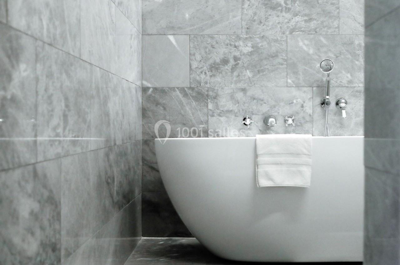 Salle de bain moderne avec baignoire blanche, murs et sol en marbre gris, serviette pliée sur le bord.